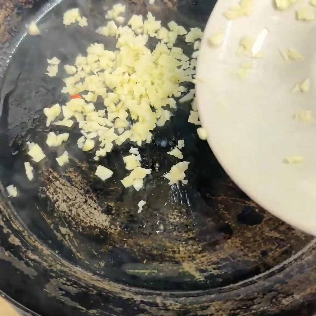 Aglio tritato versato da un piatto bianco in una padella calda.