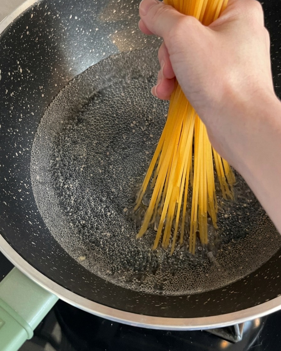 Spaghetti secchi tenuti da una mano e immersi in una pentola di acqua bollente.