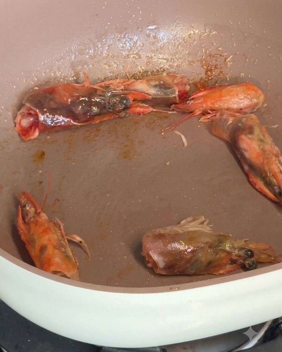 Gamberi sgusciati e teste di gamberi che sfrigolano in padella mentre vengono conditi con spezie.