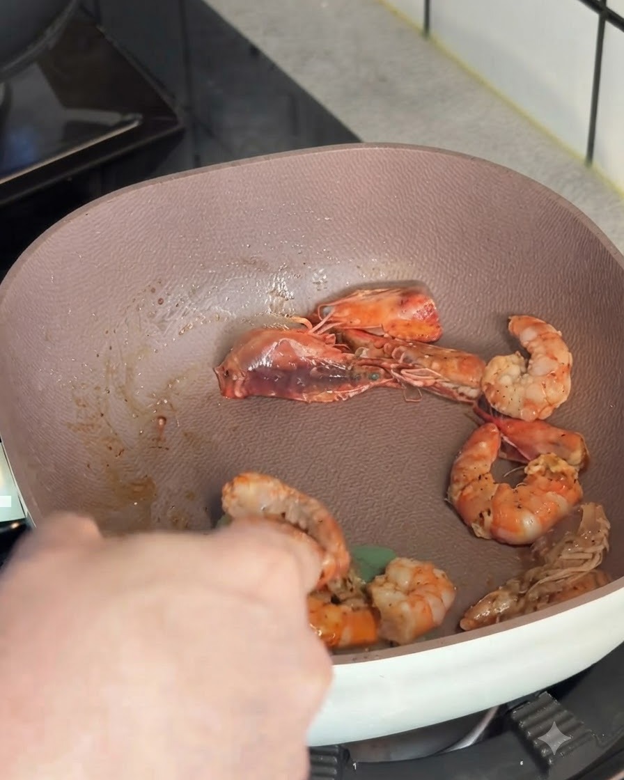Gamberi rosa saltati in padella prelevati e sollevati con un utensile da cucina.
