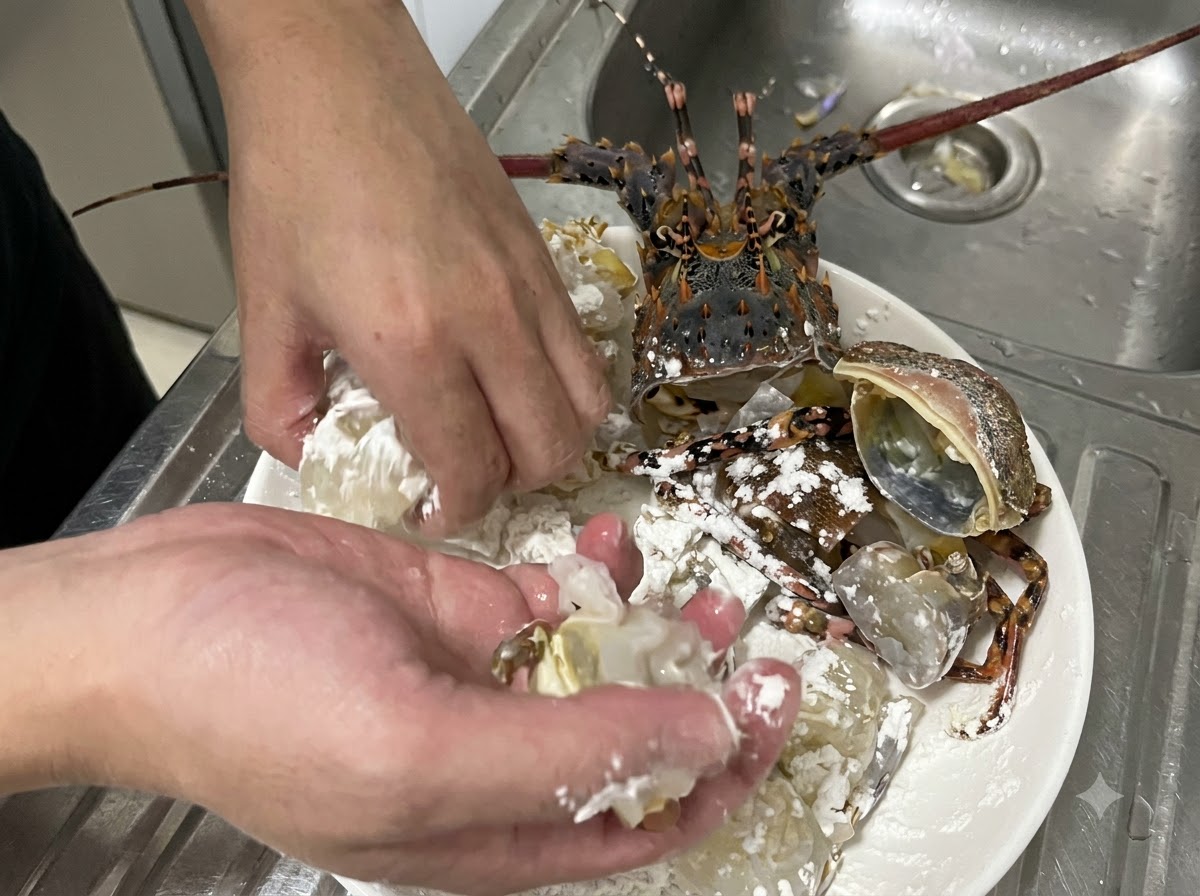 Mani che mescolano attivamente pezzi di carne di aragosta cruda e guscio nellamido di mais bianco su un piatto per assicurare una copertura uniforme.