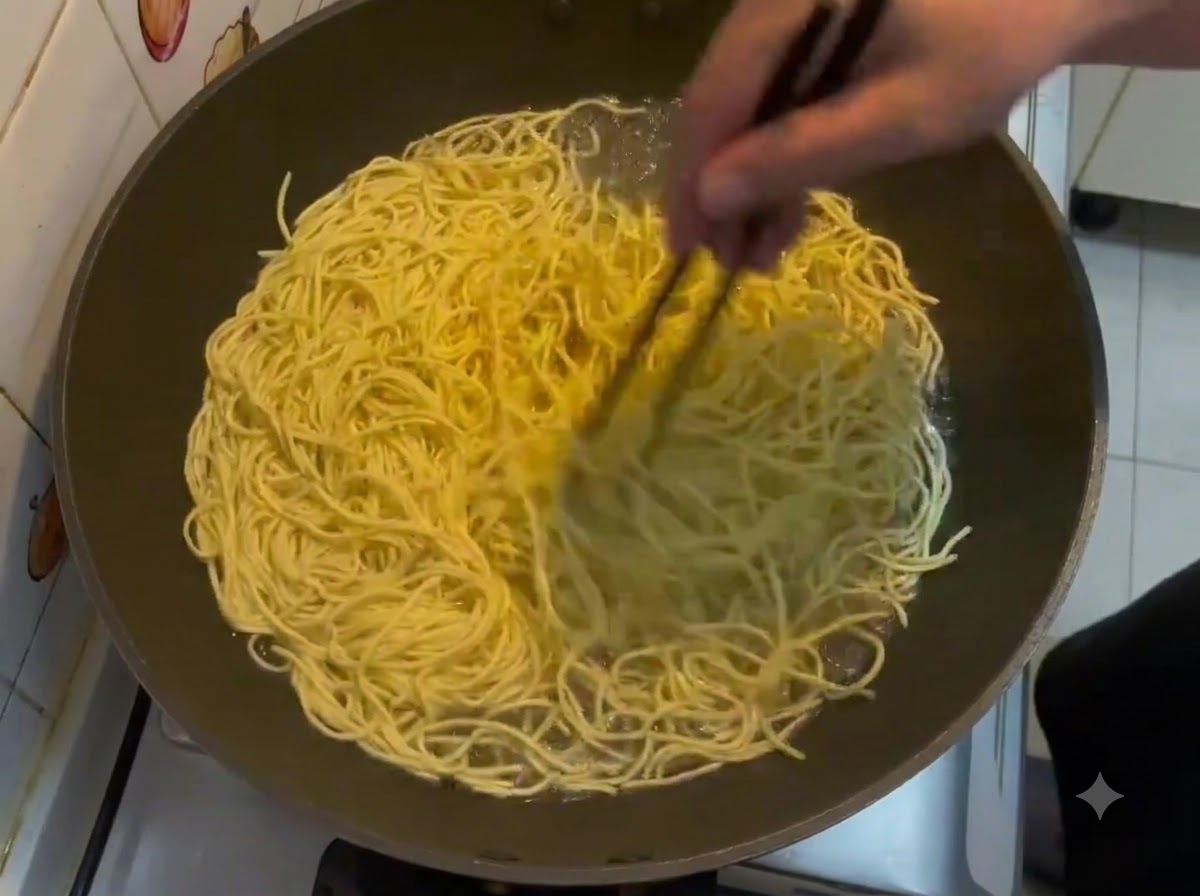 Bacchette che mescolano un grande lotto di noodles E-fu gialli in ebollizione dentro un wok.