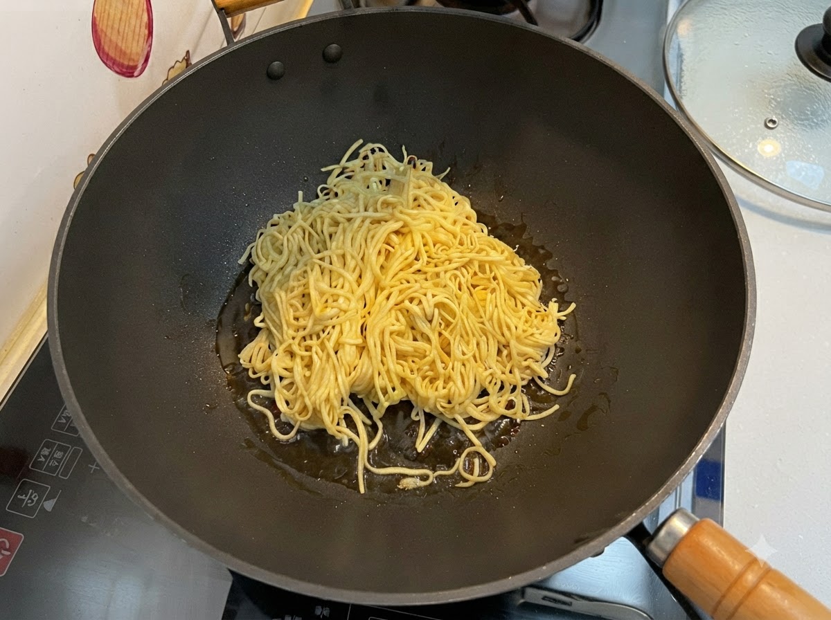 Noodles E-fu scolati che vengono saltati in un wok nero usando una spatola.