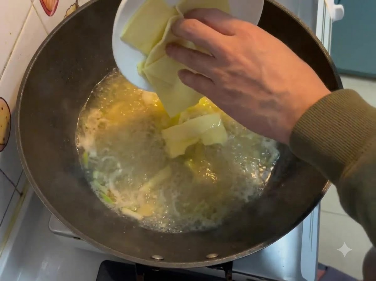 Fette di formaggio quadrate che cadono da un piatto bianco in un brodo cremoso bollente dentro un wok.