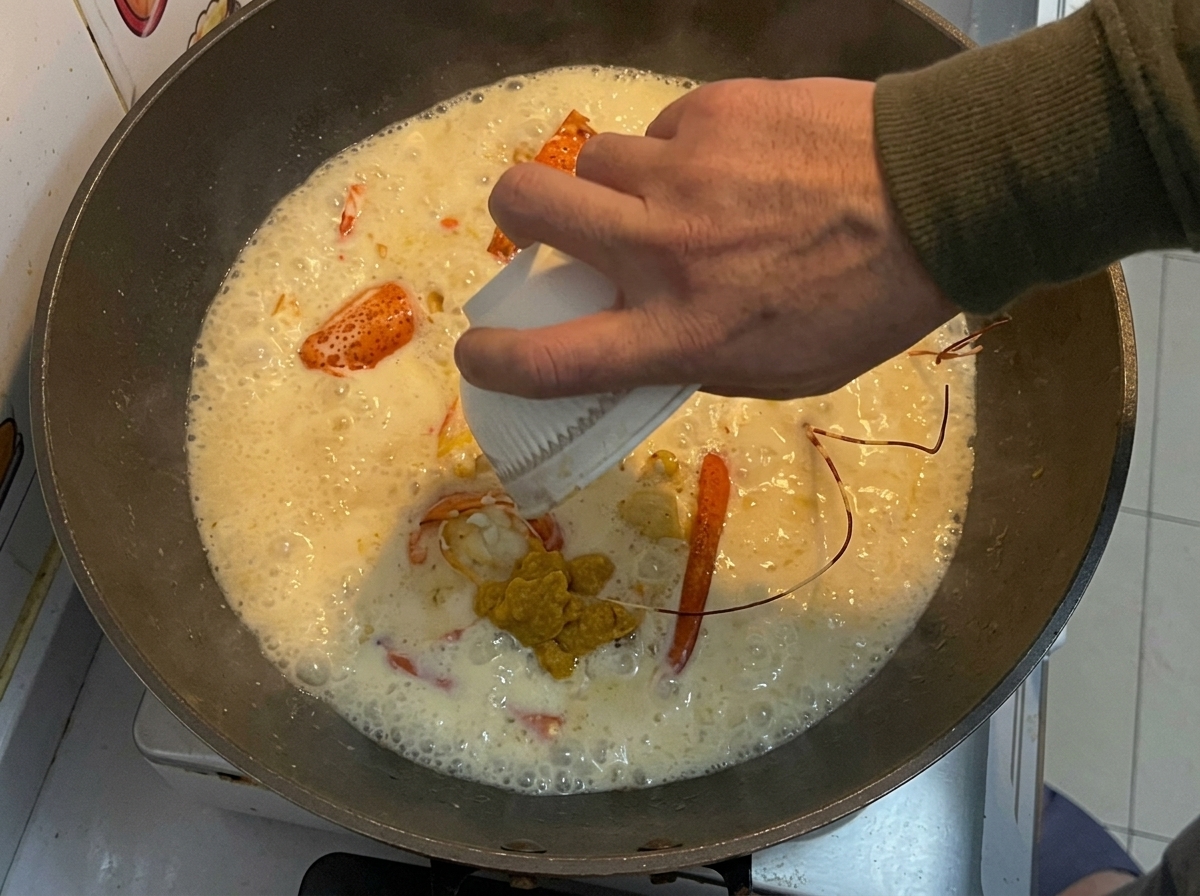 La pasta di aragosta gialla messa da parte versata da una ciotola bianca piccola in un wok con pezzi di aragosta fritti e una salsa cremosa.
