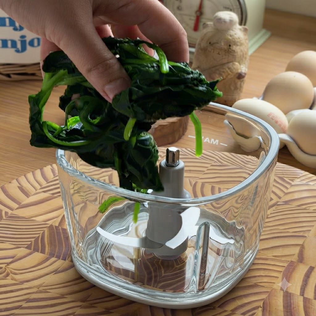 Una mano che posiziona un pugno di spinaci cotti e strizzati allinterno della ciotola di un robot da cucina in vetro.