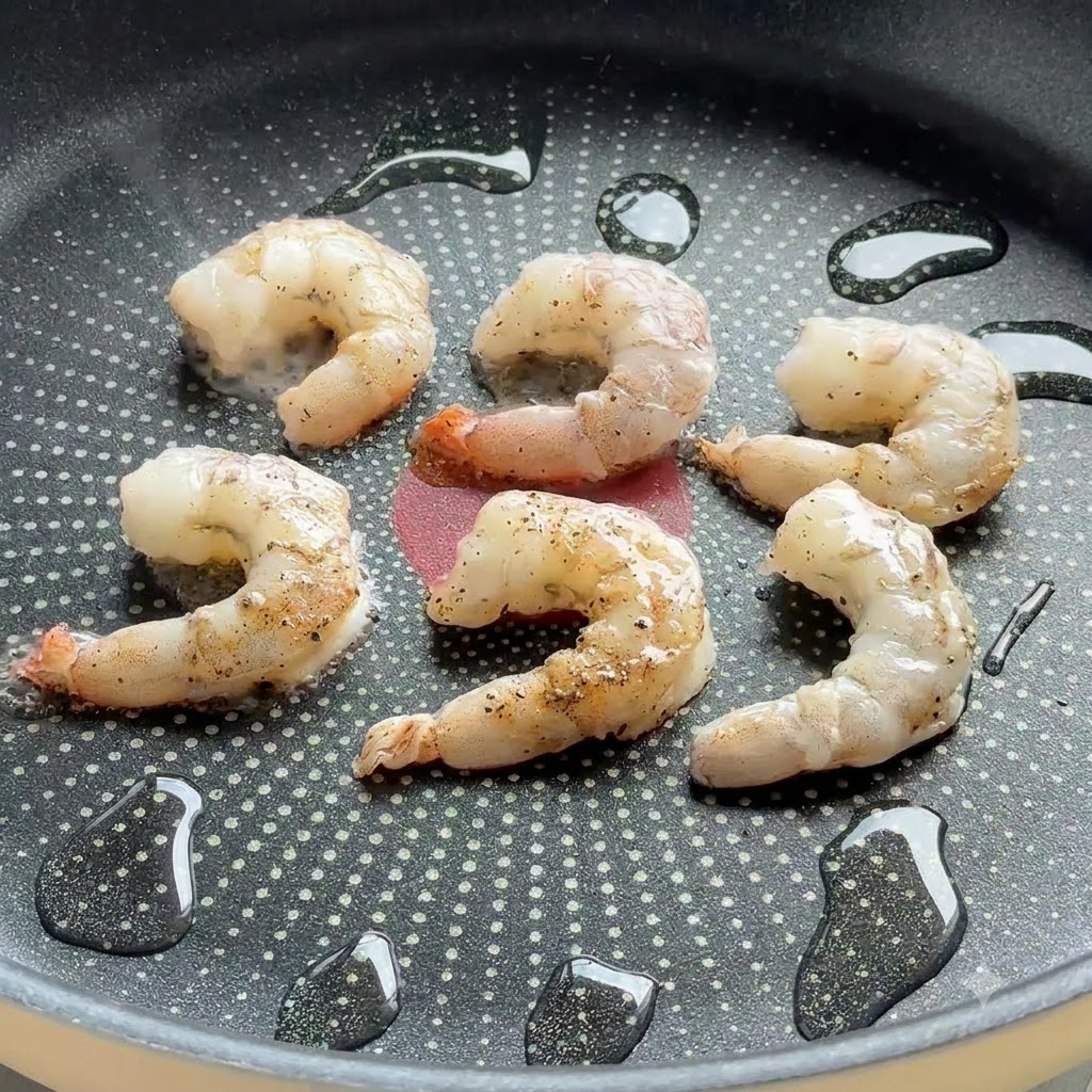 Gamberi conditi che sfrigolano in una padella antiaderente con gocce dolio.