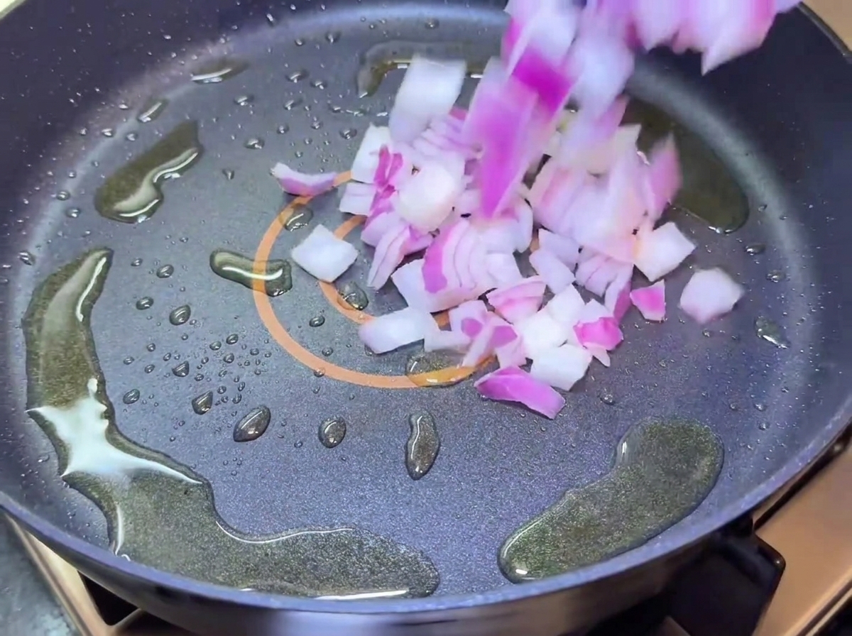 Cipolle rosse tagliate a dadini che cadono in una padella con olio.