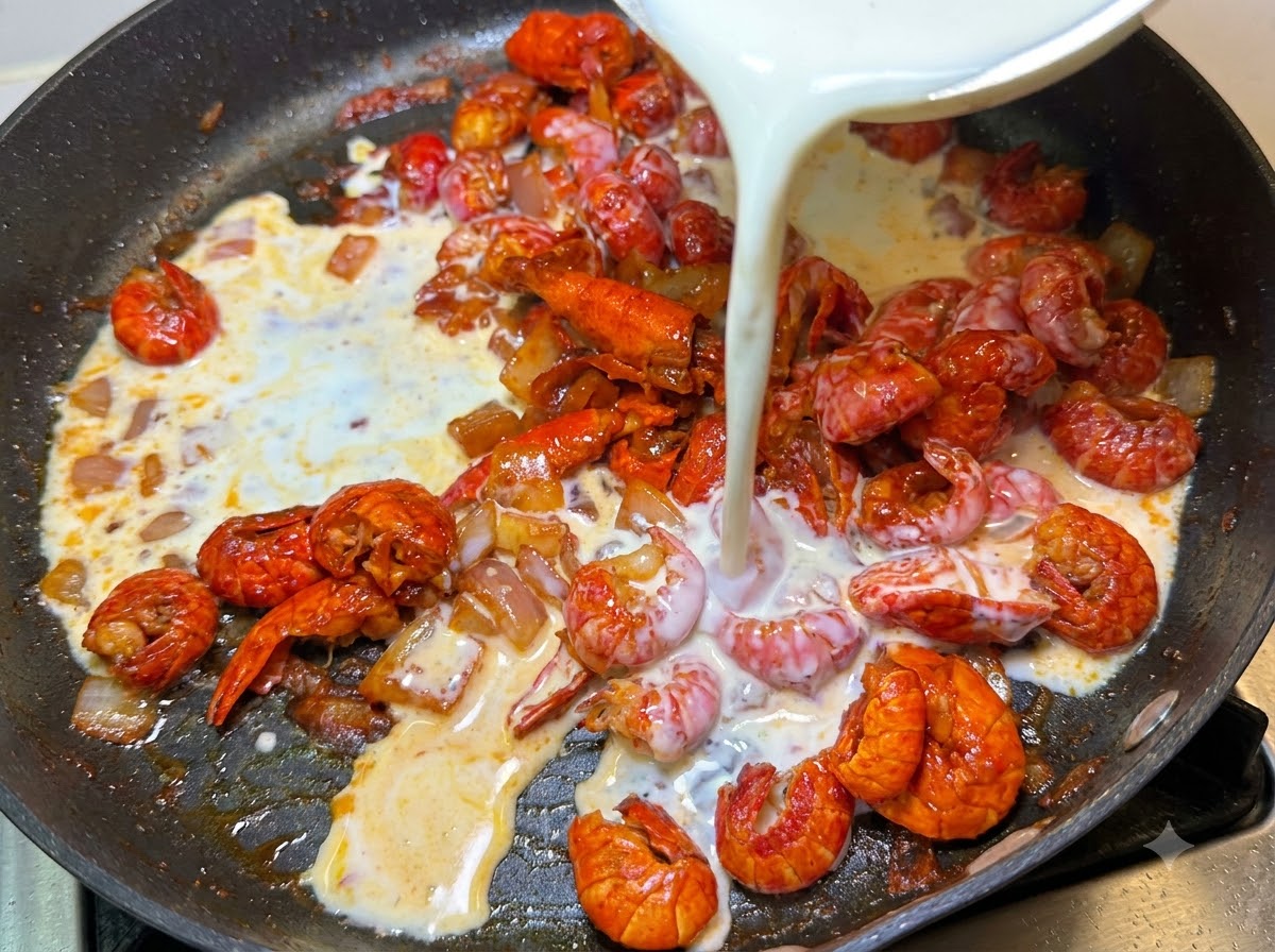 Latte e panna da montare versati da una ciotola nella padella contenente i gamberi e le cipolle.