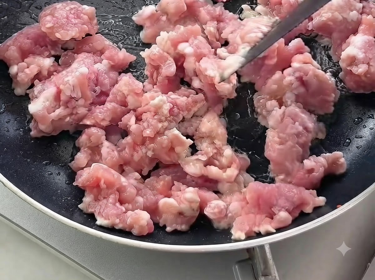 Carne di maiale macinata cruda mescolata e cotta in una padella nera.