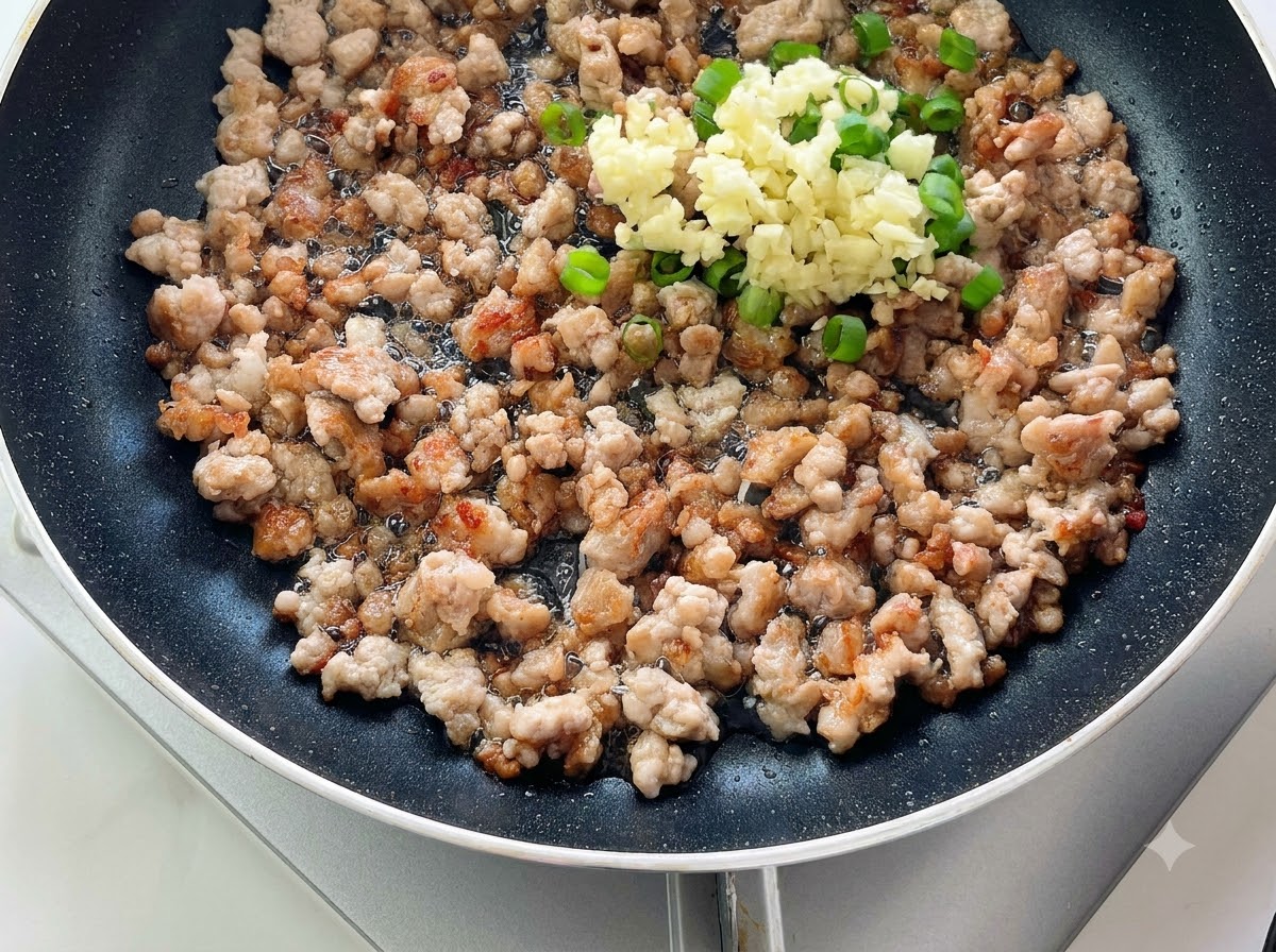 Aglio tritato e cipolle verdi ammucchiati sopra la carne macinata cotta in una padella.