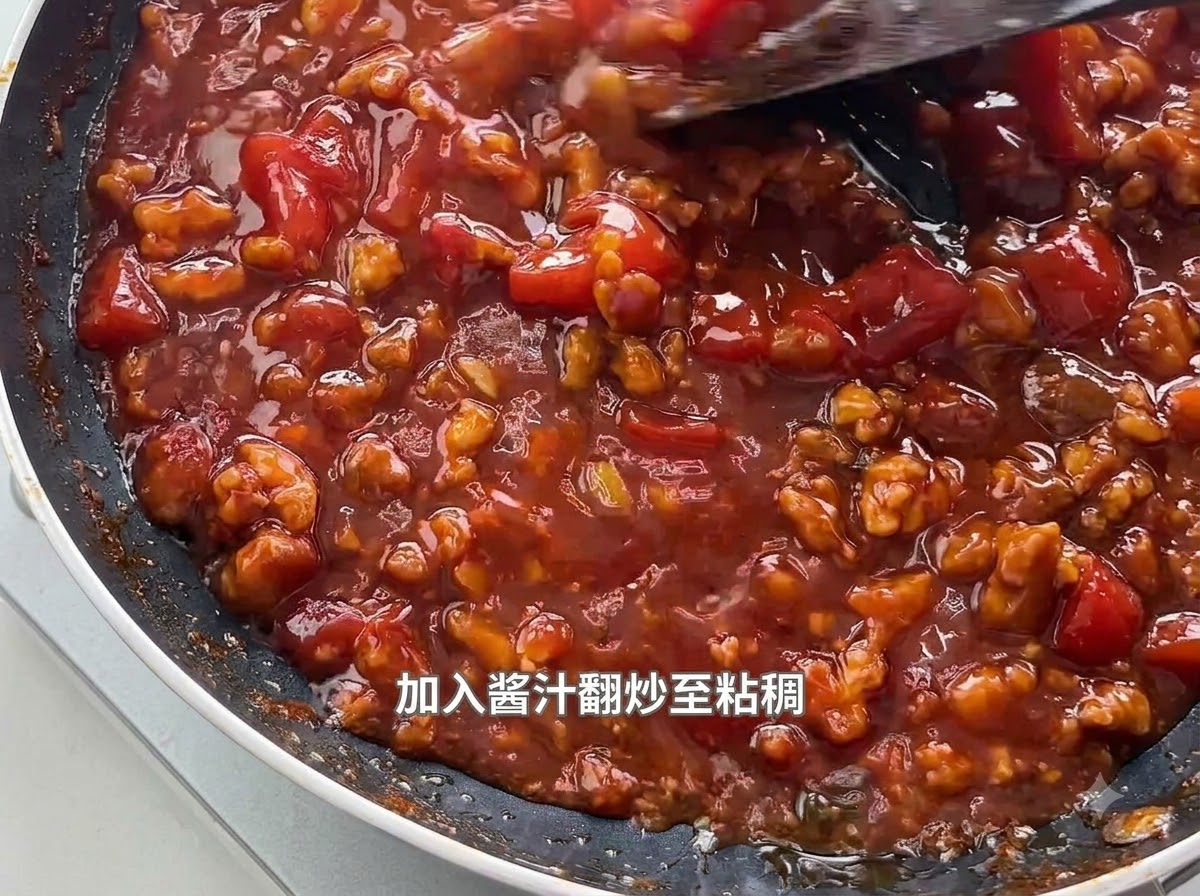Una spatola che mescola una salsa densa, ribollente di pomodoro e carne macinata in una padella nera.