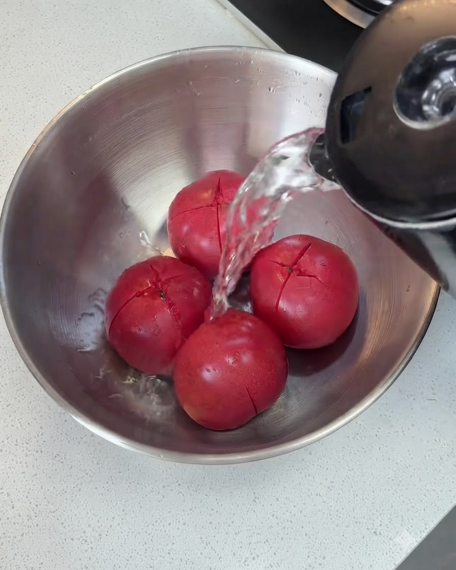 Acqua calda versata da un bollitore sui pomodori incisi in una ciotola di metallo.
