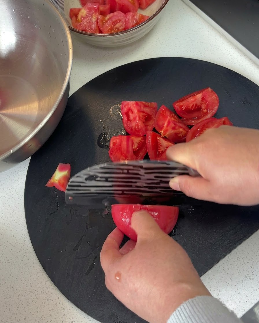 Pomodori pelati tagliati a pezzi su un tagliere scuro con un coltello.