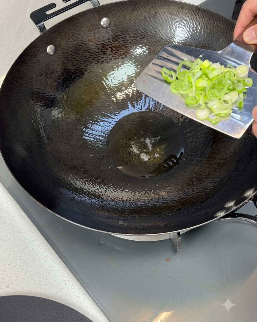 Cipollotti tritati buttati in un wok caldo pieno di olio da cucina scintillante.