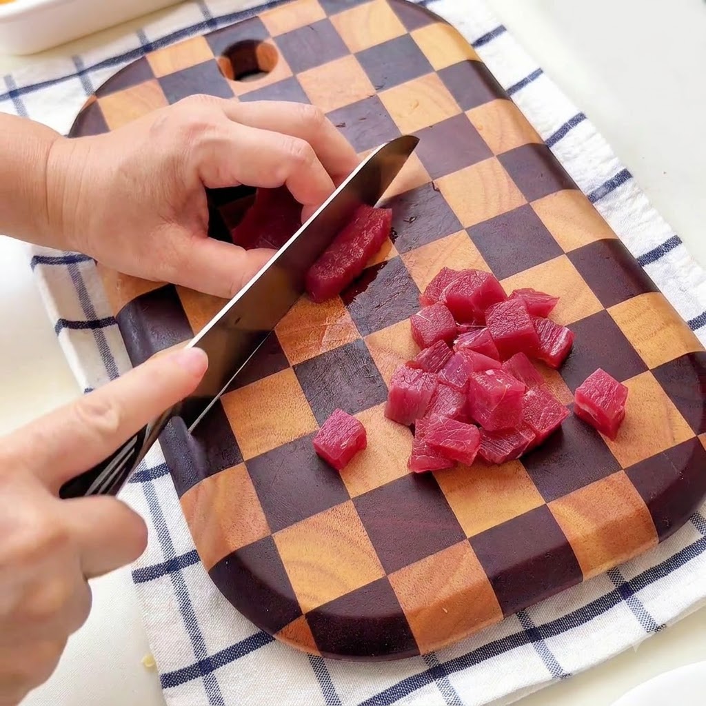 Una persona che taglia il manzo a piccoli cubetti su un tagliere di legno a scacchi.