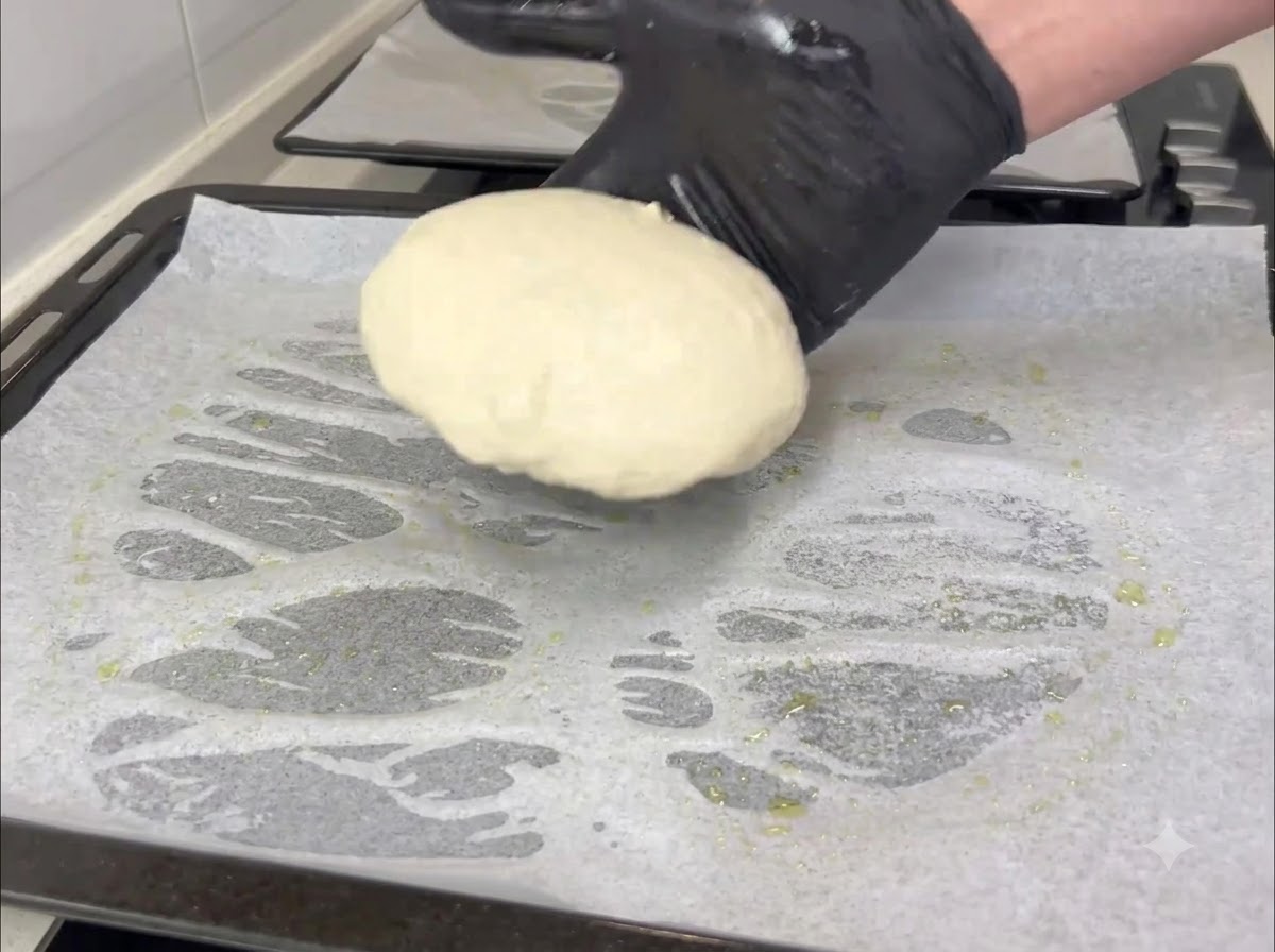 Una mano guantata che trasferisce una piccola porzione rotonda di impasto su una teglia foderata di carta forno.