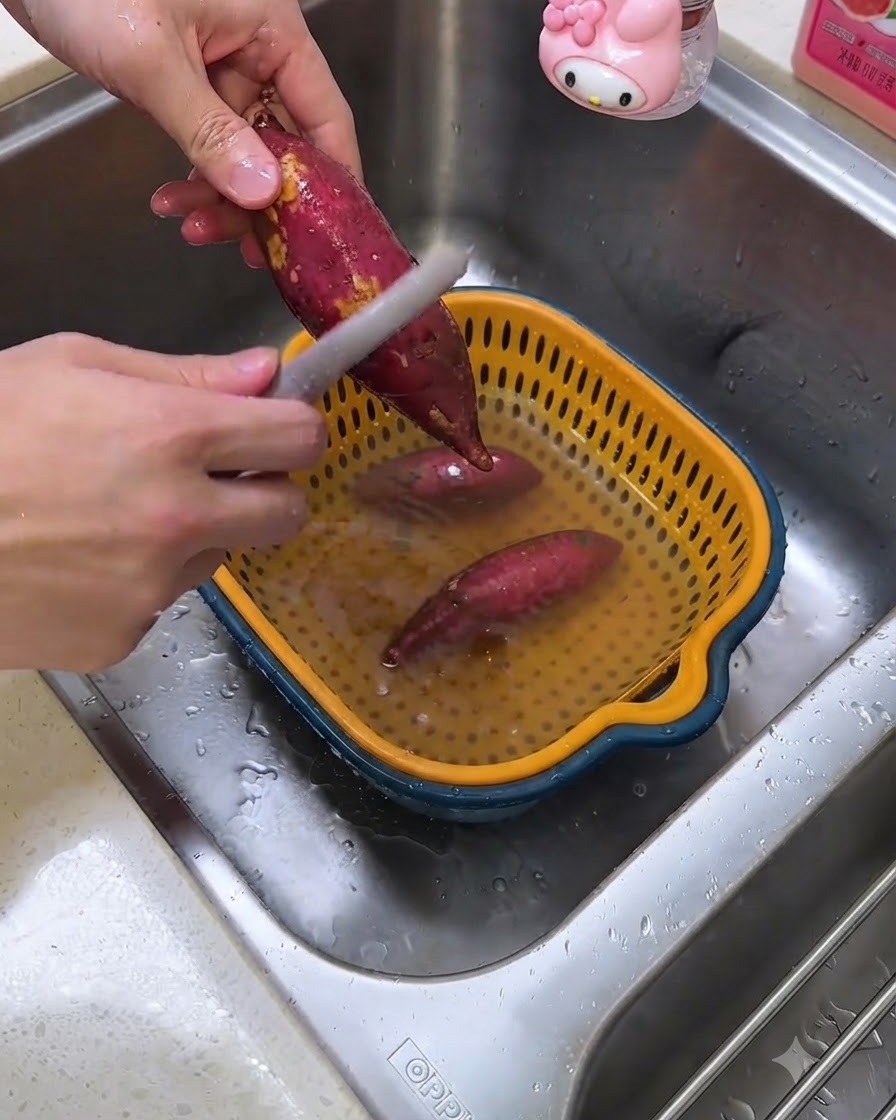 Una persona che pela patate dolci crude sopra un lavandino usando un pelapatate.