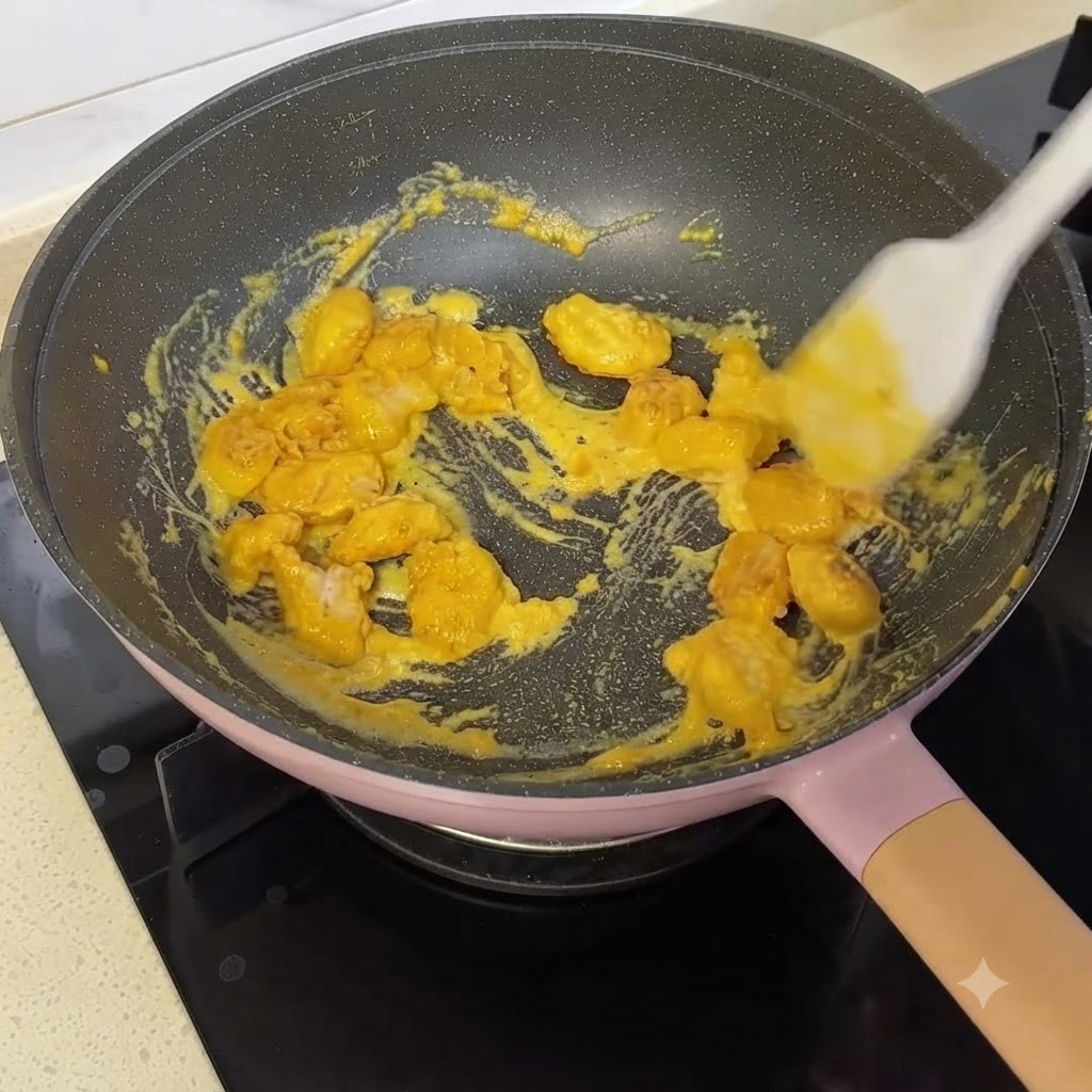 Bocconcini di pollo mescolati e ricoperti con salsa gialla al tuorlo duovo salato in una padella usando una spatola in silicone.