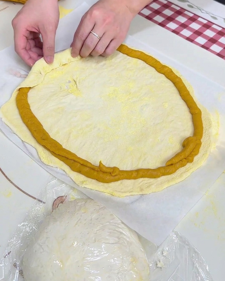 Mani che ripiegano il bordo dellimpasto sopra lanello di purea di patate dolci su carta da forno.