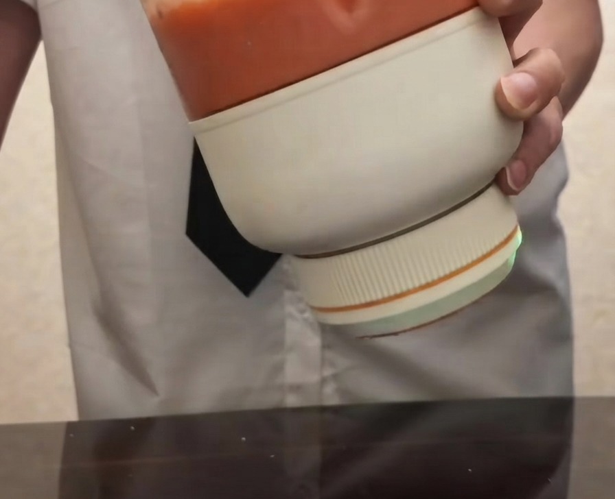 Una persona che tiene un frullatore elettrico portatile riempito di purea di pomodoro rosso brillante e liscia.