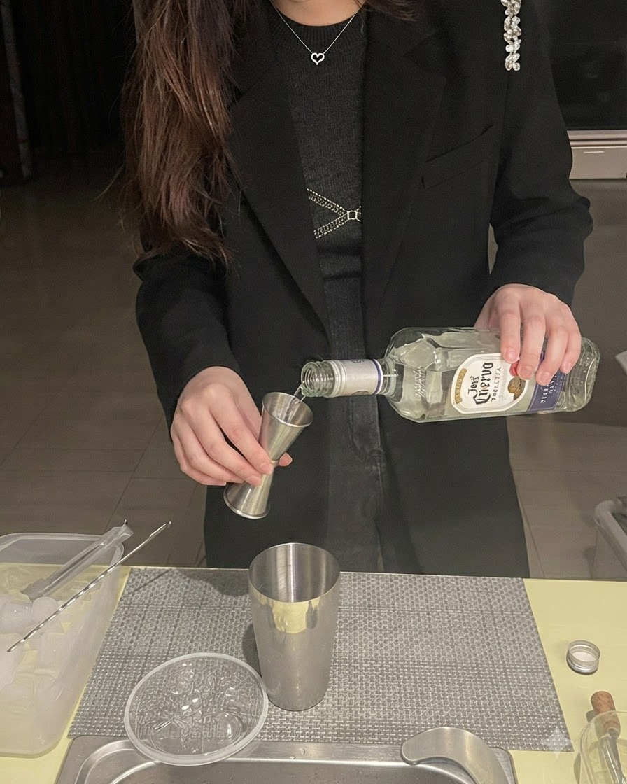 Tequila versata da una bottiglia in un dosatore jigger posizionato sopra uno shaker di metallo.