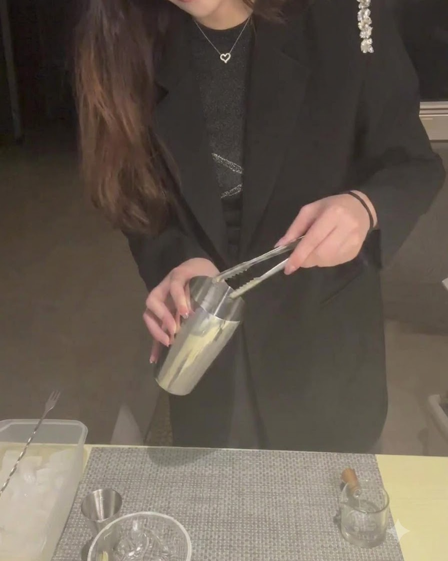 Una persona che utilizza le pinze per mettere i cubetti di ghiaccio in un bricco dello shaker in metallo.