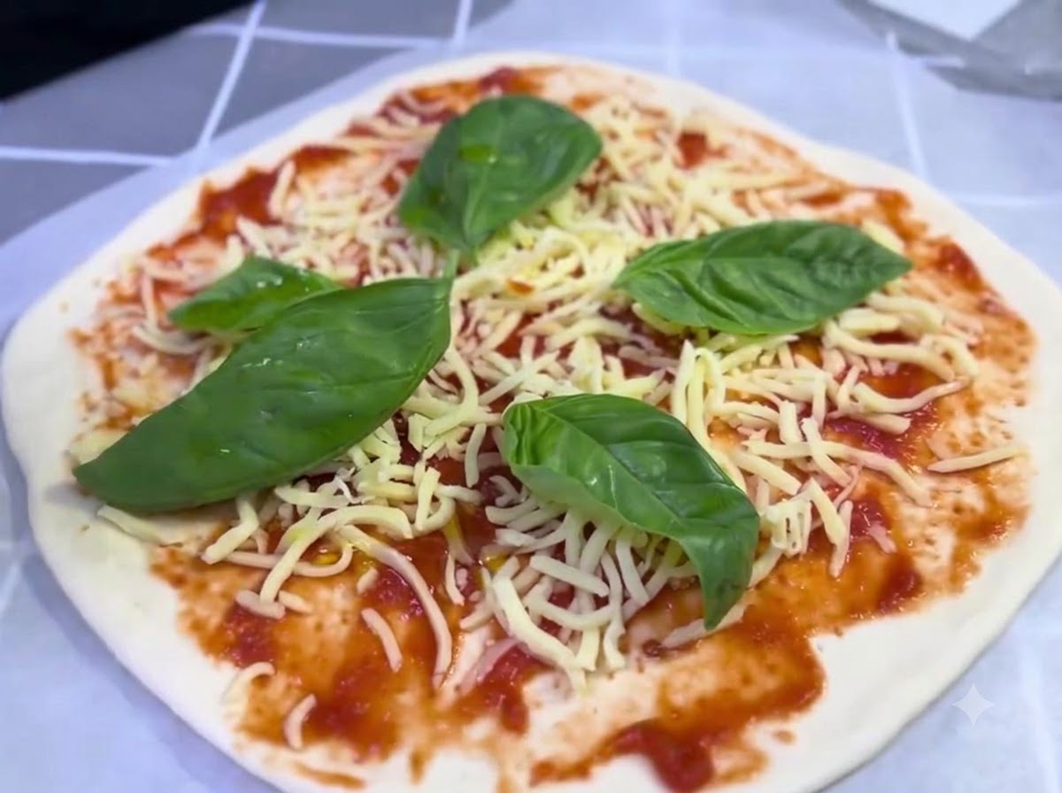 Una pizza assemblata guarnita con formaggio e foglie di basilico che riceve un leggero filo dolio doliva.