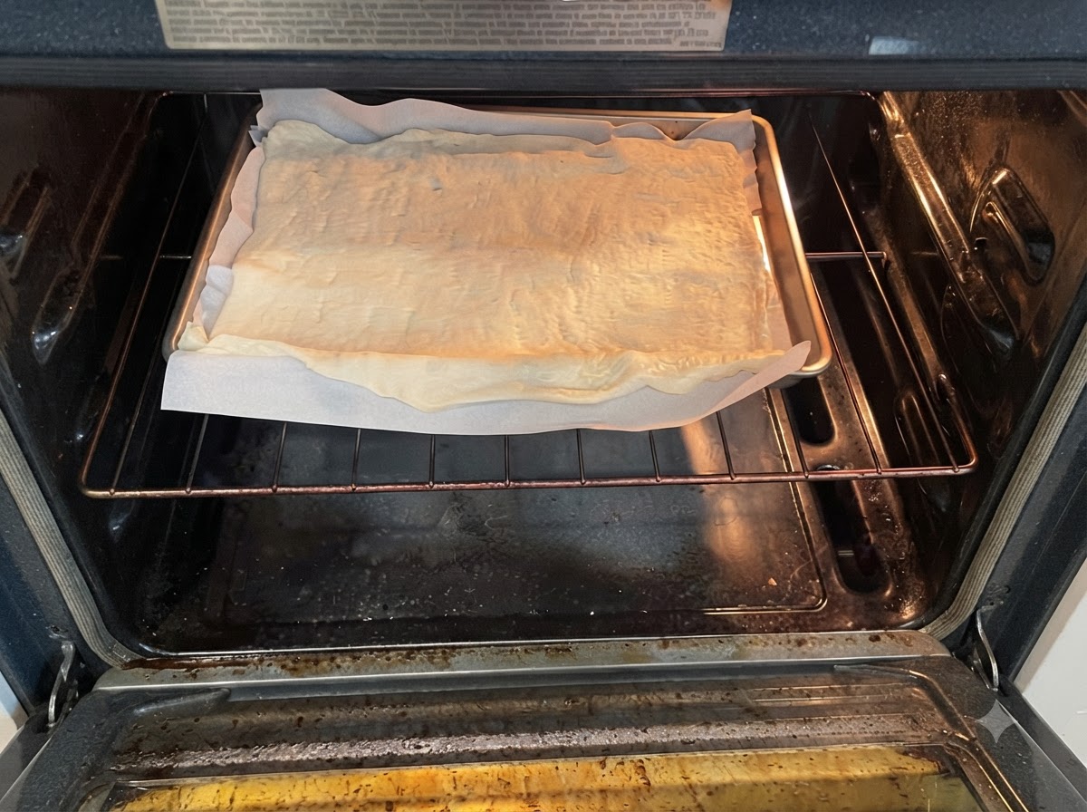 Una teglia con limpasto crudo della pizza su carta da forno posizionata sulla griglia allinterno di un forno preriscaldato.