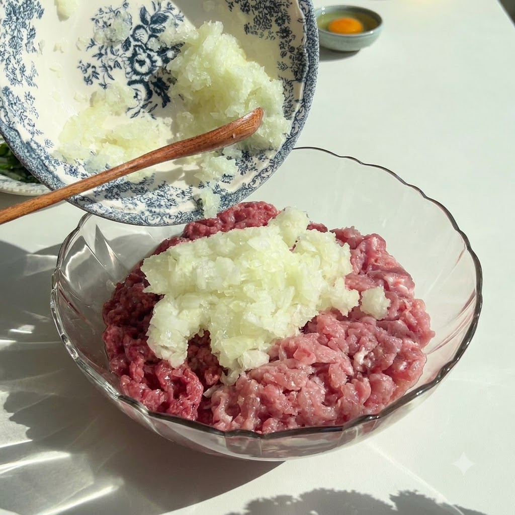 Cipolle e prezzemolo tritati finemente versati da una ciotola decorativa in una ciotola di vetro contenente carne macinata cruda.
