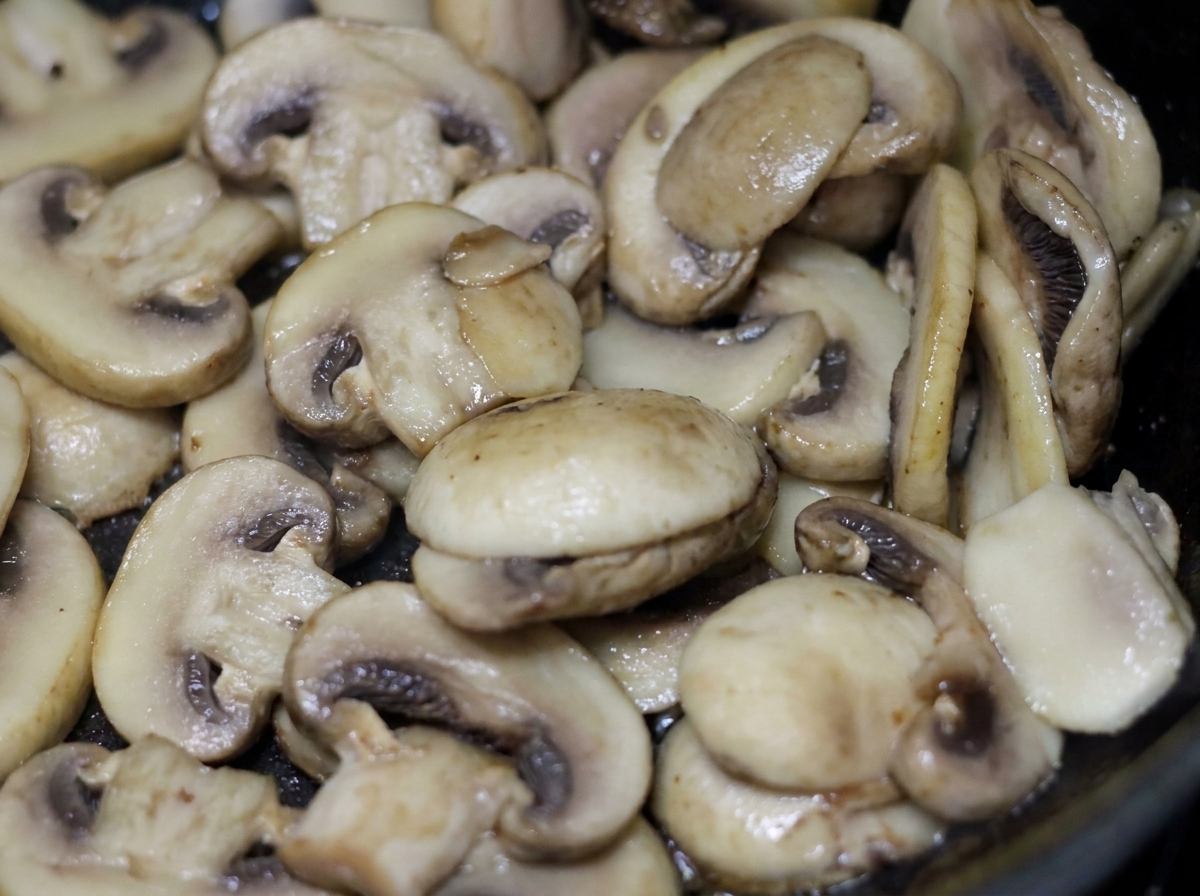 Funghi champignon bianchi affettati che sfrigolano e cuociono in padella con panna leggera.