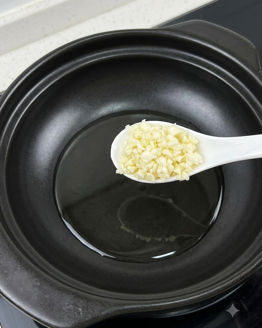 Un cucchiaio di aglio tritato tenuto sopra una pentola accanto a un tuorlo duovo separato.