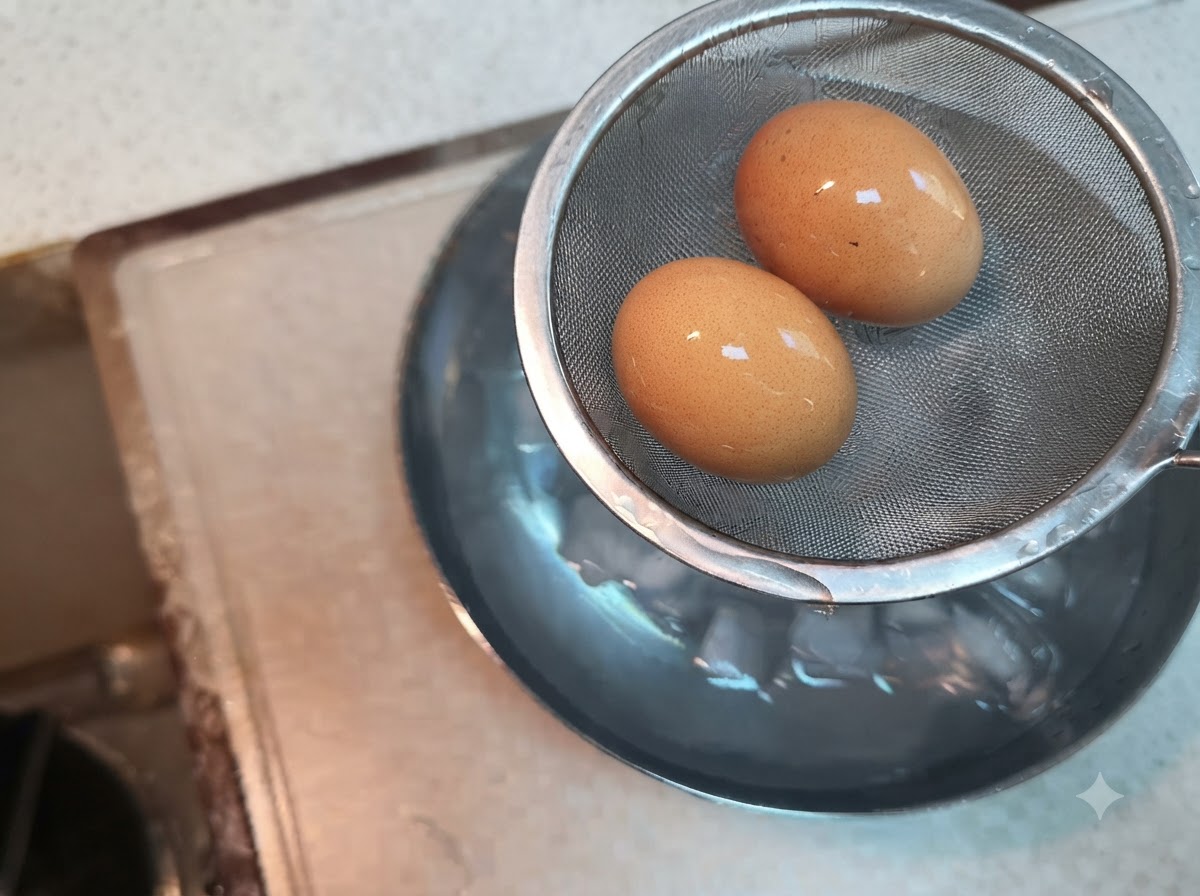 Due uova sode in un colino di metallo tenuto sopra una ciotola di acqua e ghiaccio.