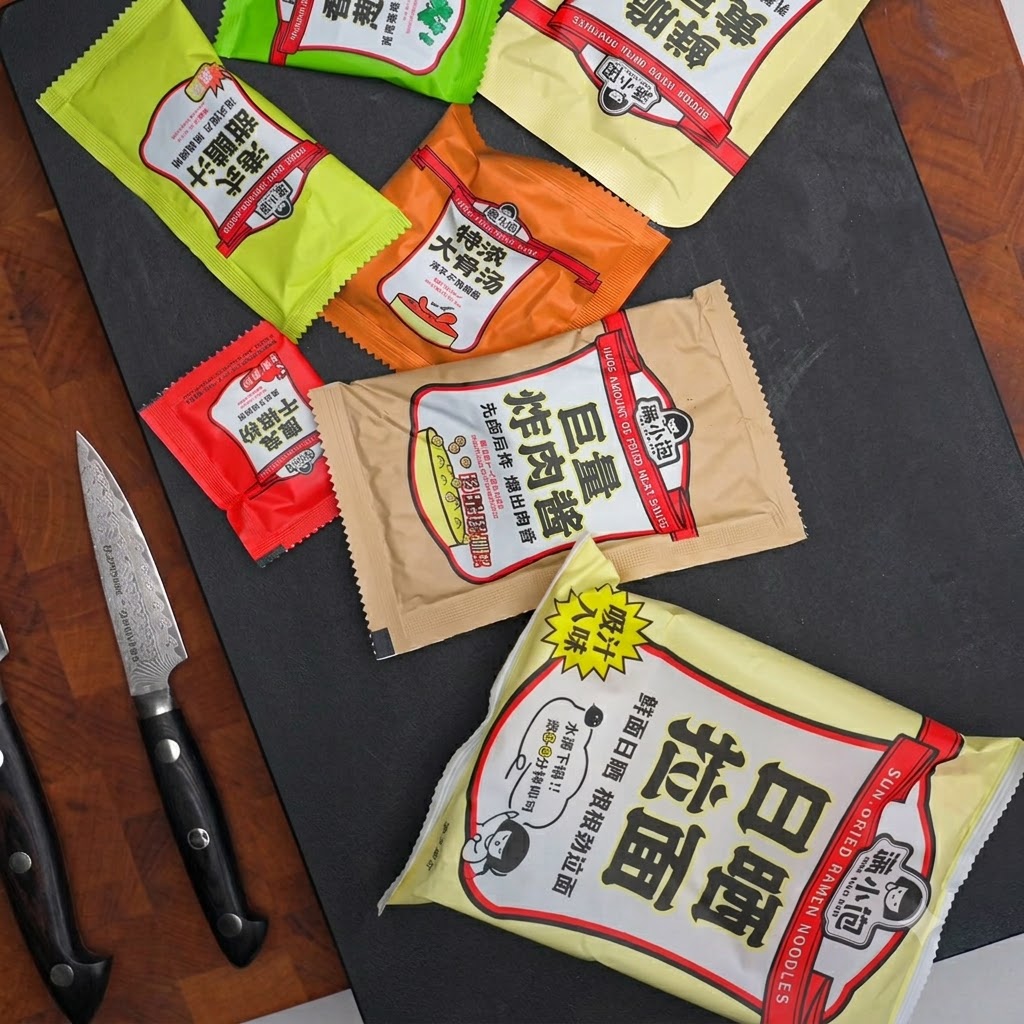 Varie bustine di condimento, bustine di salsa e un coltello disposti su una superficie scura.