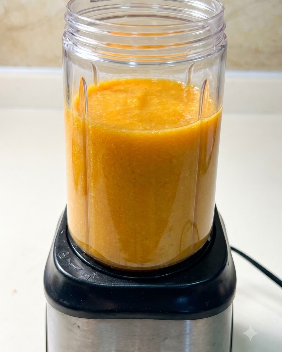 Un bicchiere del frullatore riempito con un composto di zuppa arancione posizionato sopra una base motore nera.