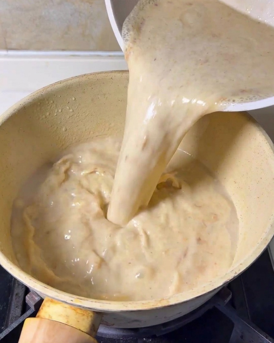 Base per zuppa cremosa e frullata versata da un contenitore in una pentola gialla sui fornelli.