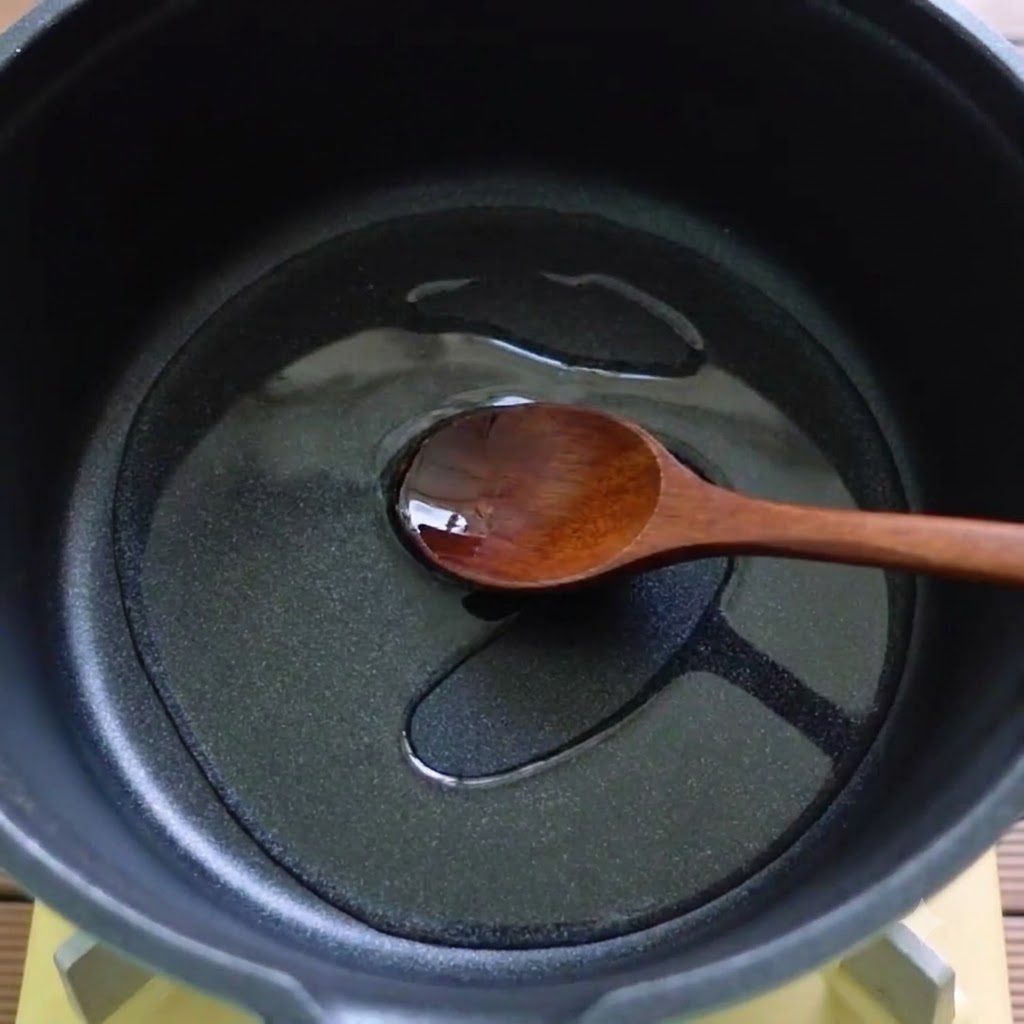Un cucchiaio di legno che mescola olio e ingredienti sciolti in una pentola nera.