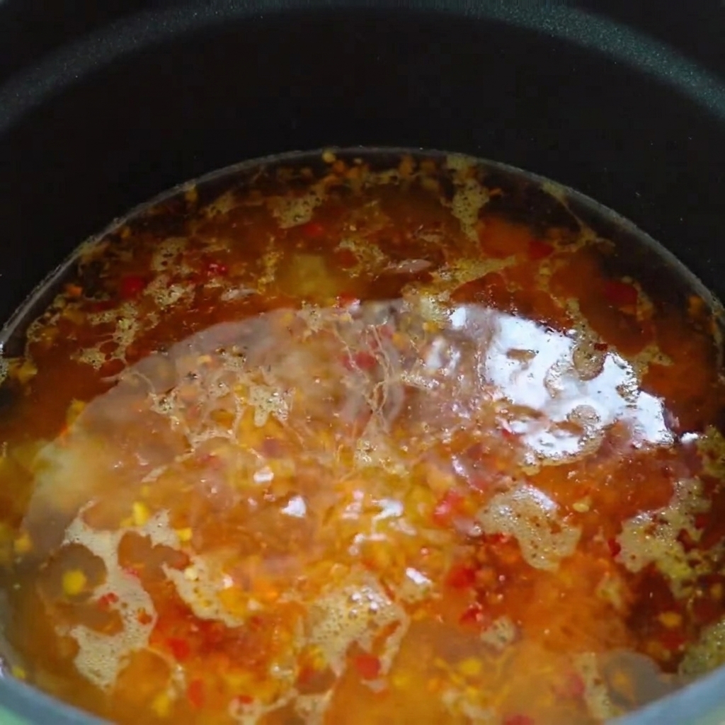 Olio piccante e olio di sesamo fatti gocciolare sulla superficie della base della zuppa calda.