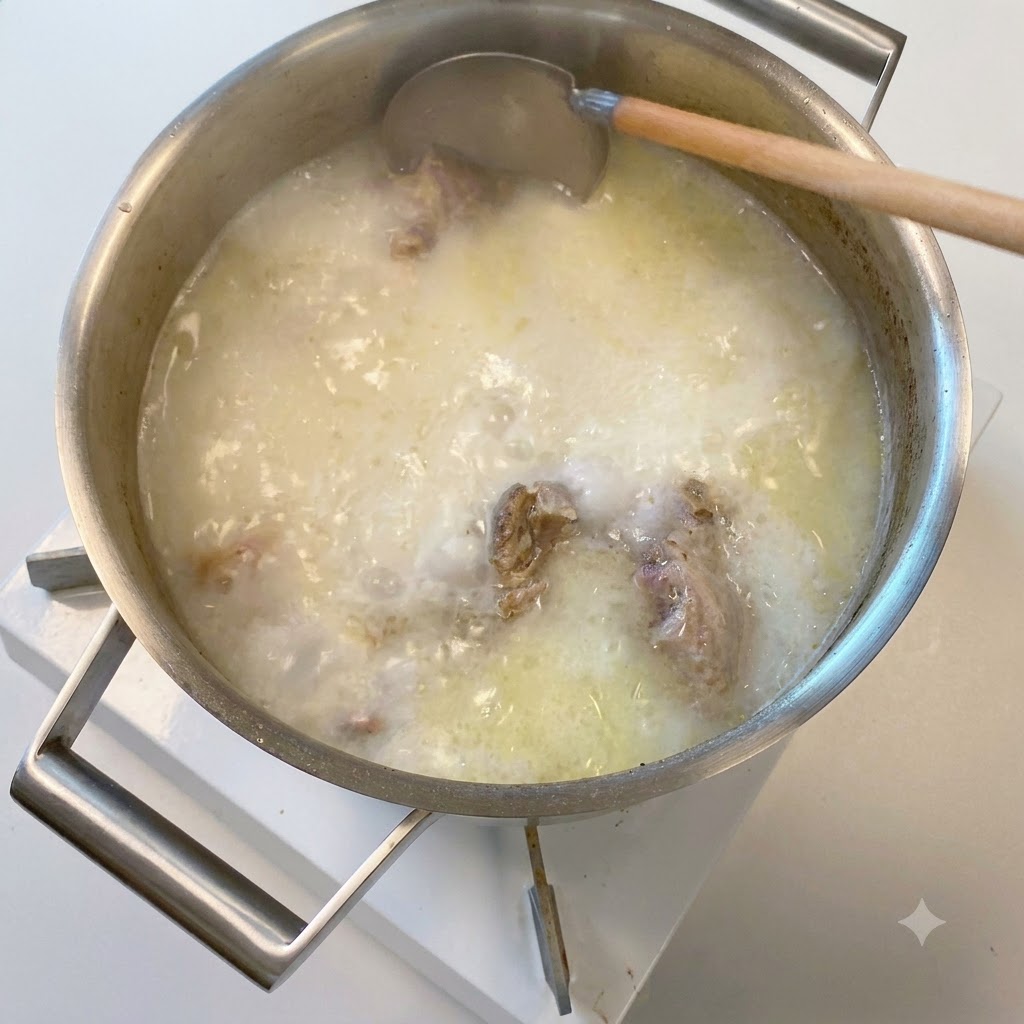 Un metolo di legno che immerge in una pentola di brodo di ossa di maiale bollente opaco e bianco lattiginoso.