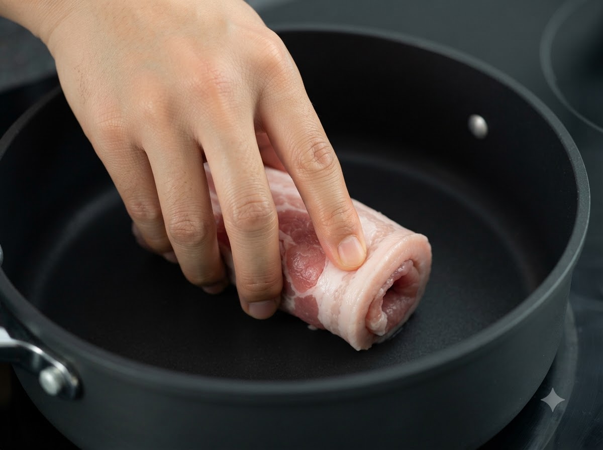 Il rotolo di pancetta di maiale legato mentre viene scottato in una padella scura sul fuoco.