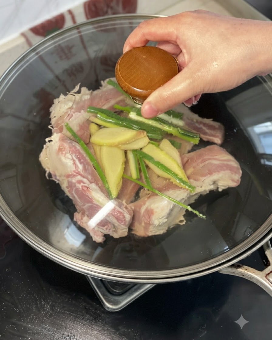 Una mano che versa del vino giallo sulle costolette di manzo, zenzero e cipollotti in un wok.