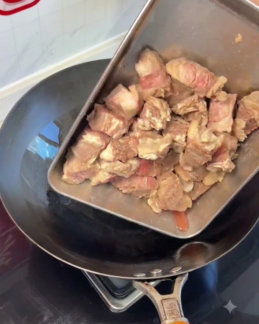 Pezzi di costolette di manzo sbollentate versati da un vassoio dacciaio in un wok caldo.