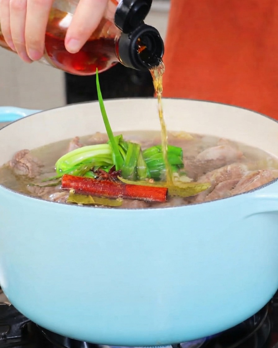 Vino da cucina versato da una bottiglietta in una pentola da stufato dai toni chiari.