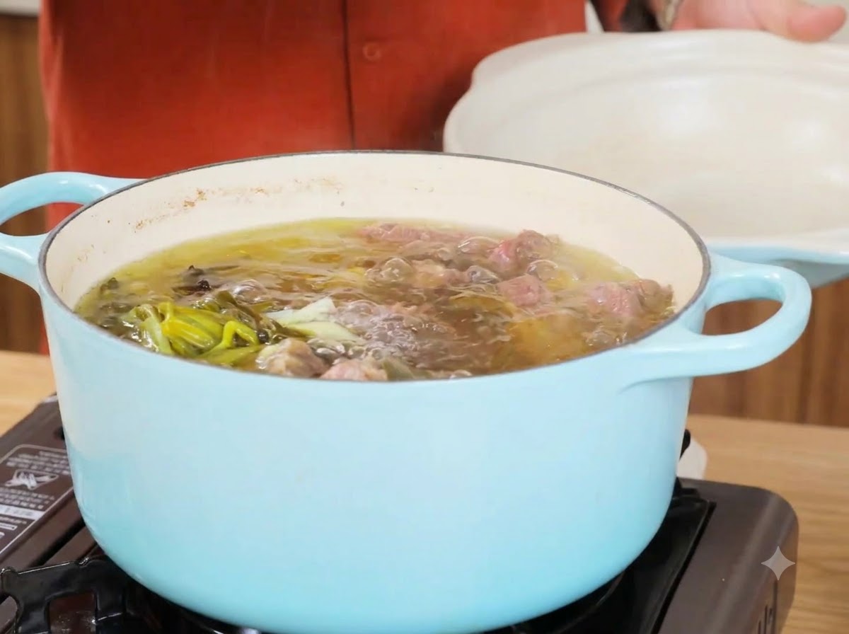 Una pentola di brodo di manzo in ebollizione dopo aver rimosso gli ingredienti principali, mostrando liquido chiaro e cipollotti.