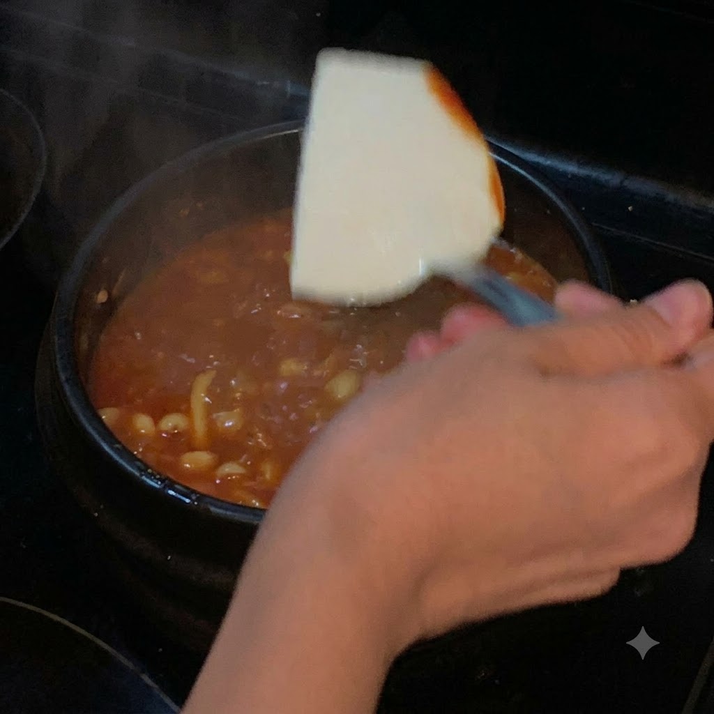 Una fetta di tofu morbido calata con una spatola in una pentola di zuppa rossa bollente.