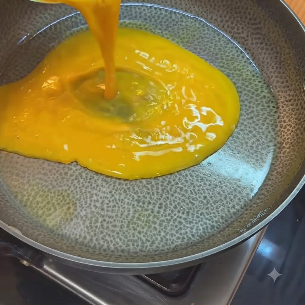 Uova sbattute giallo brillante versate da un misurino in una padella calda unta dolio.