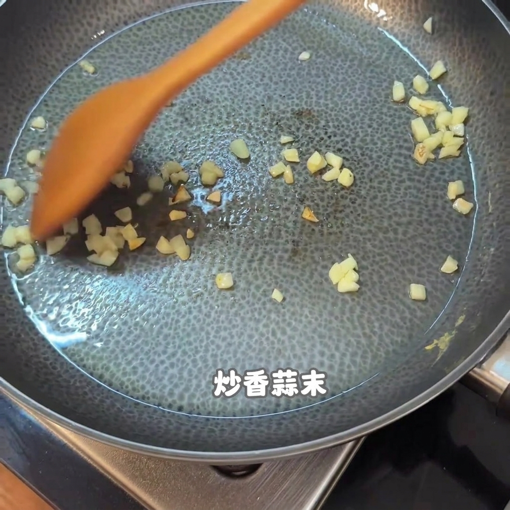Aglio tritato e pezzetti di cibo mescolati con una spatola di legno arancione in una padella antiaderente.