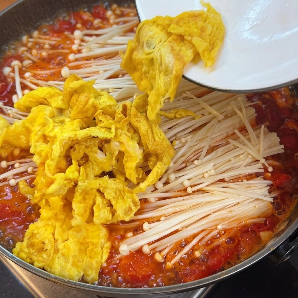 Cubetti di tofu tenero aggiunti nella pentola contenente brodo di pomodoro, funghi e uova.