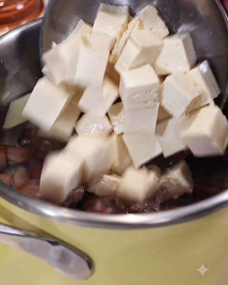 Tofu a cubetti fatto scivolare da una schiumarola in una pentola di acqua bollente con zenzero e vongole.