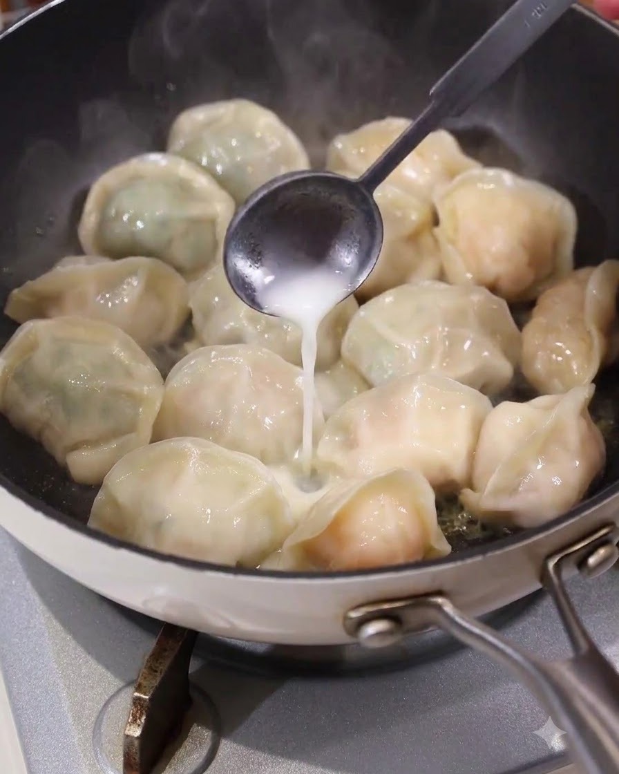 Un cucchiaio che versa una pastella liquida bianca in modo uniforme negli spazi tra i ravioli in una padella calda.